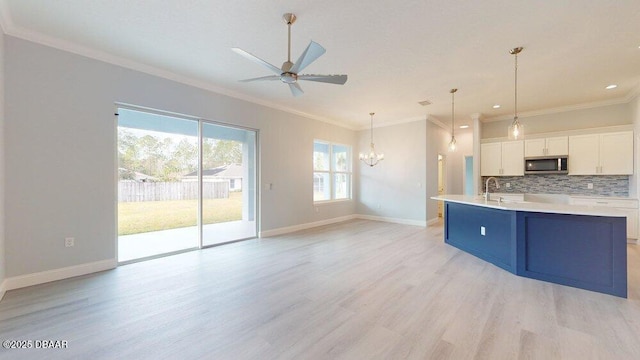 kitchen with crown molding, tasteful backsplash, decorative light fixtures, a center island with sink, and white cabinets