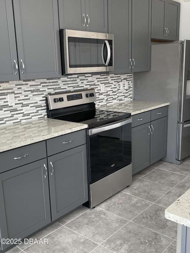 kitchen featuring light stone countertops, appliances with stainless steel finishes, decorative backsplash, light tile patterned floors, and gray cabinetry