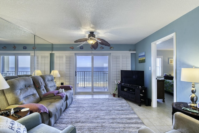 tiled living room featuring a water view, ceiling fan, and a textured ceiling