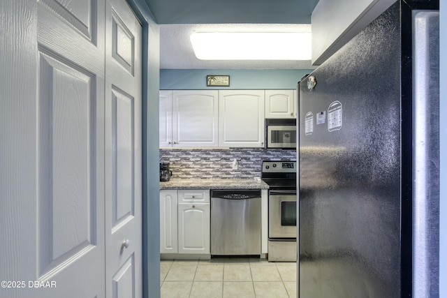 kitchen featuring light tile patterned floors, white cabinetry, appliances with stainless steel finishes, backsplash, and dark stone counters