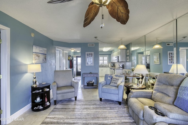 living room with ceiling fan, sink, a wood stove, a textured ceiling, and light tile patterned floors