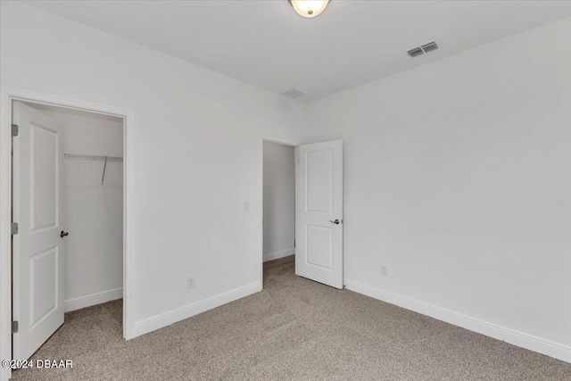 unfurnished bedroom with a walk in closet, light carpet, and a closet