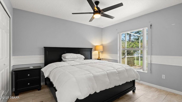 bedroom featuring a textured ceiling, a wainscoted wall, a closet, and a ceiling fan