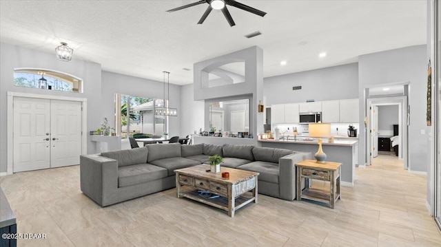 living area featuring recessed lighting, ceiling fan with notable chandelier, a towering ceiling, baseboards, and visible vents