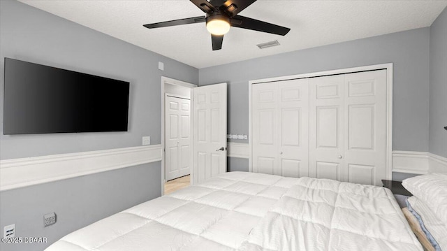 bedroom featuring a textured ceiling, visible vents, a ceiling fan, a closet, and wainscoting