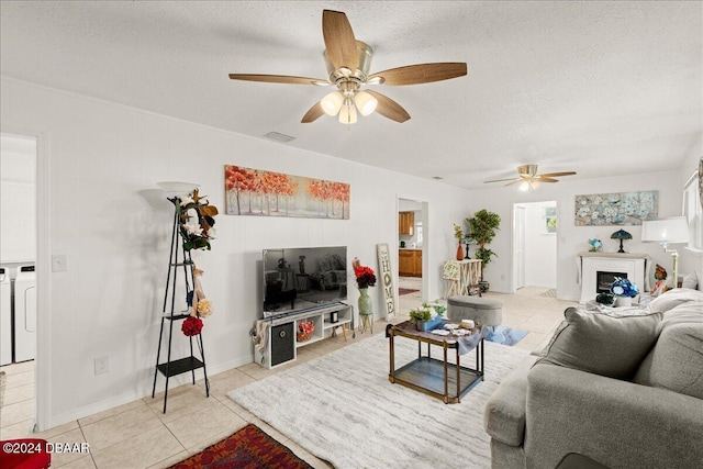 living room featuring ceiling fan, a textured ceiling, light tile patterned floors, and washer and clothes dryer