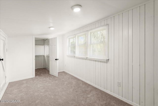 unfurnished bedroom with wooden walls, light carpet, and a closet