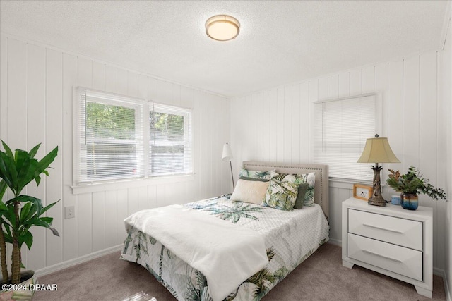 bedroom with wooden walls, a textured ceiling, and carpet flooring