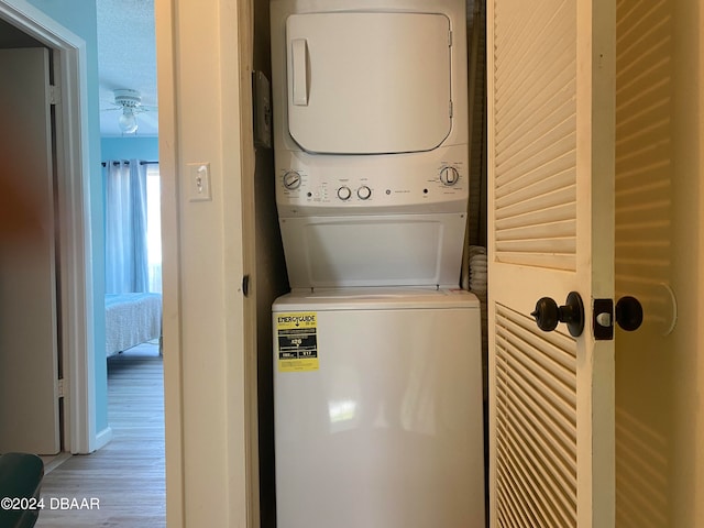 clothes washing area featuring ceiling fan, stacked washing maching and dryer, wood-type flooring, and a textured ceiling