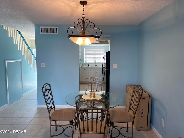 tiled dining area featuring sink, a textured ceiling, and a notable chandelier