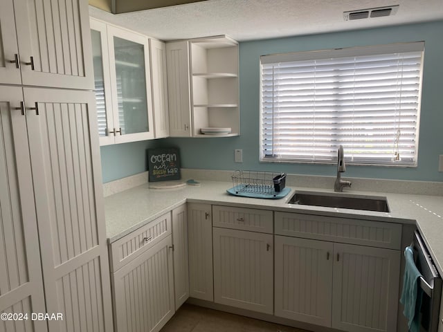 kitchen with stainless steel dishwasher, sink, tile patterned floors, and a textured ceiling