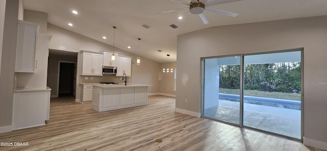 kitchen with decorative light fixtures, white cabinetry, light countertops, stainless steel microwave, and a center island with sink