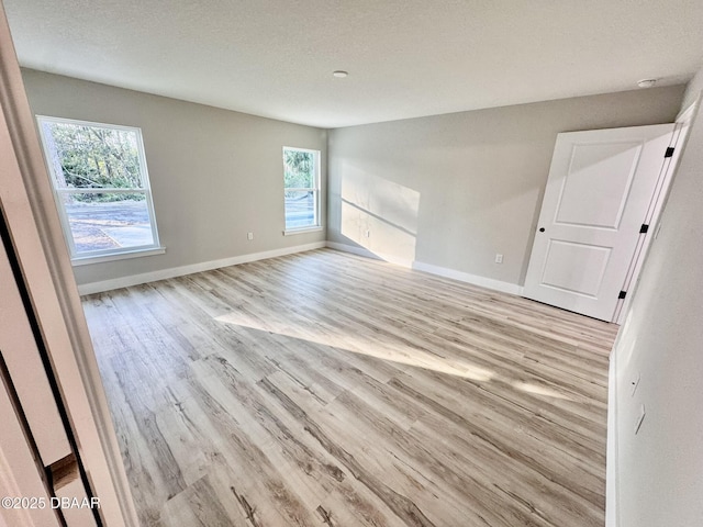 empty room featuring light wood-style floors, a textured ceiling, and baseboards