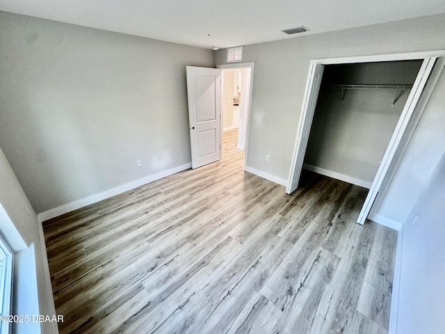 unfurnished bedroom featuring light wood finished floors, baseboards, visible vents, and a closet