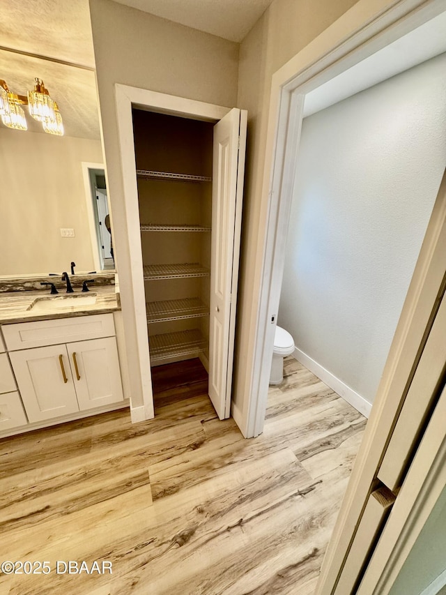 bathroom with a walk in closet, toilet, vanity, wood finished floors, and baseboards