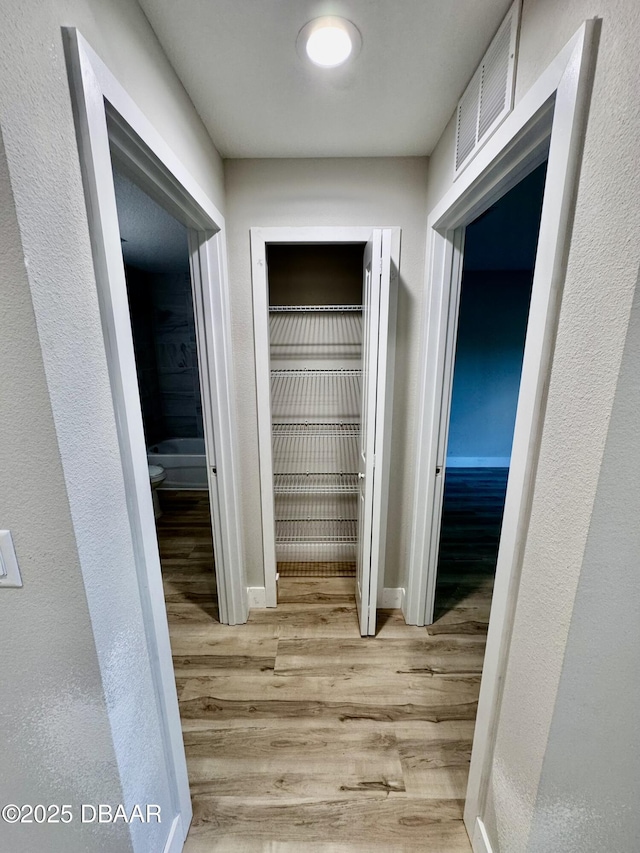 corridor with baseboards, visible vents, and wood finished floors