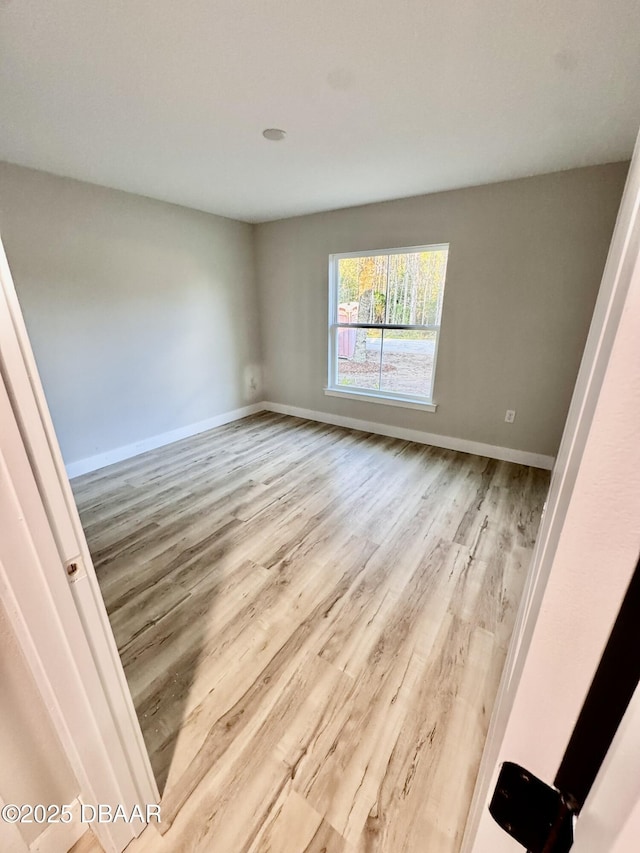 spare room featuring baseboards and light wood-style floors