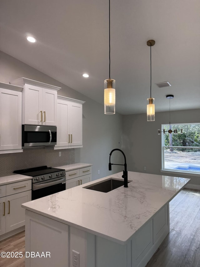 kitchen featuring pendant lighting, stainless steel appliances, white cabinets, a sink, and light stone countertops