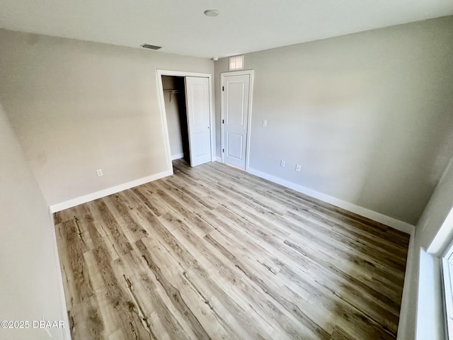 unfurnished bedroom featuring light wood finished floors, baseboards, visible vents, and a closet