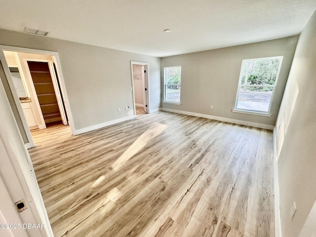 interior space featuring light wood-style floors, visible vents, a spacious closet, and baseboards