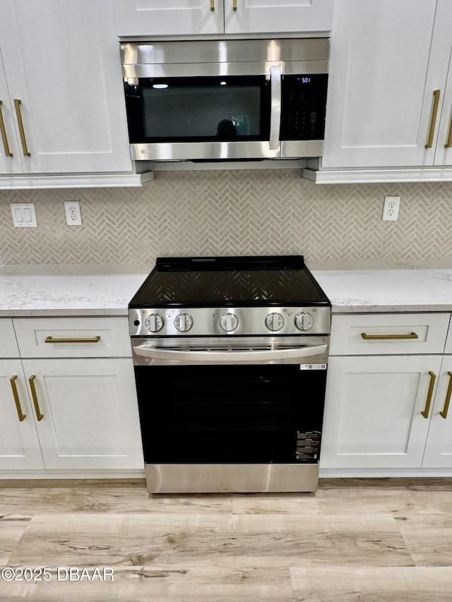 kitchen featuring appliances with stainless steel finishes, light wood-type flooring, white cabinets, and light stone countertops