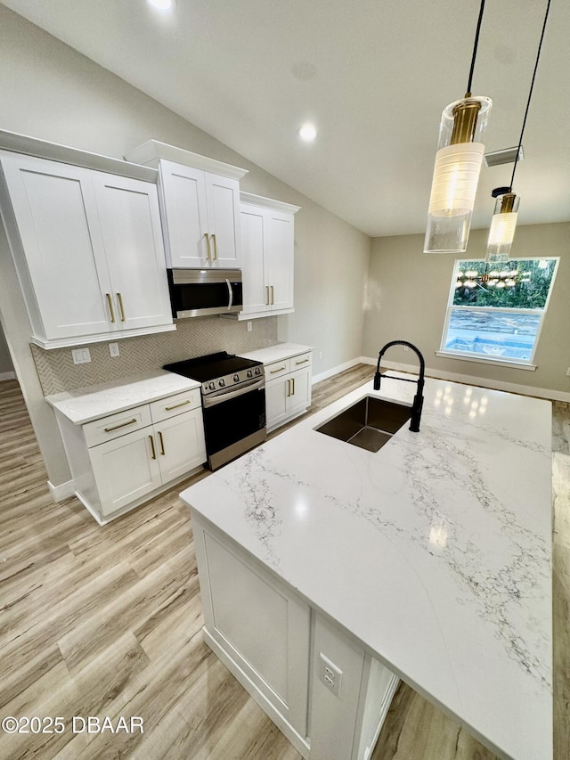 kitchen with light stone counters, stainless steel appliances, a sink, white cabinets, and pendant lighting