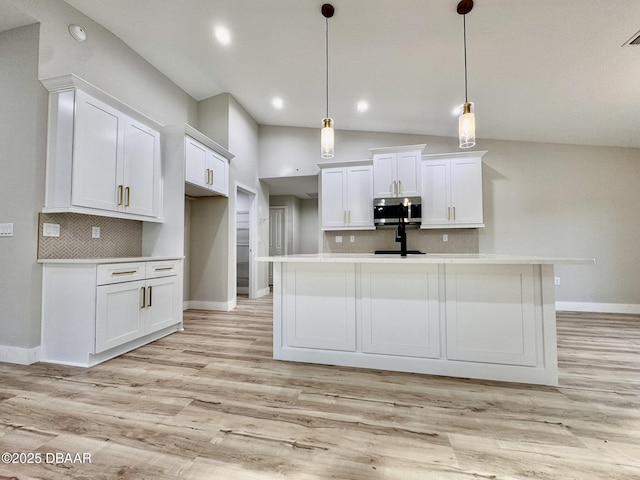 kitchen featuring a kitchen island with sink, hanging light fixtures, stainless steel microwave, and white cabinetry