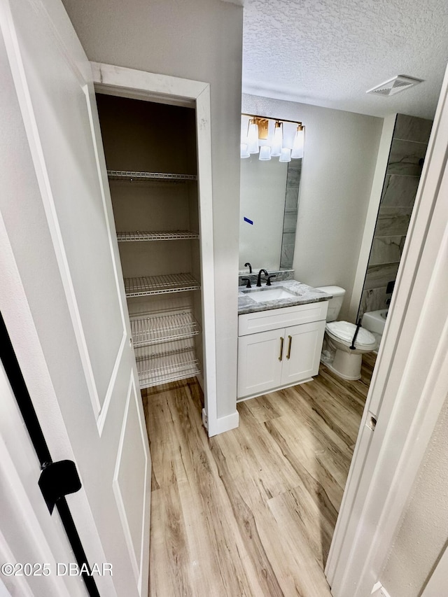 bathroom with visible vents, toilet, vanity, a textured ceiling, and wood finished floors