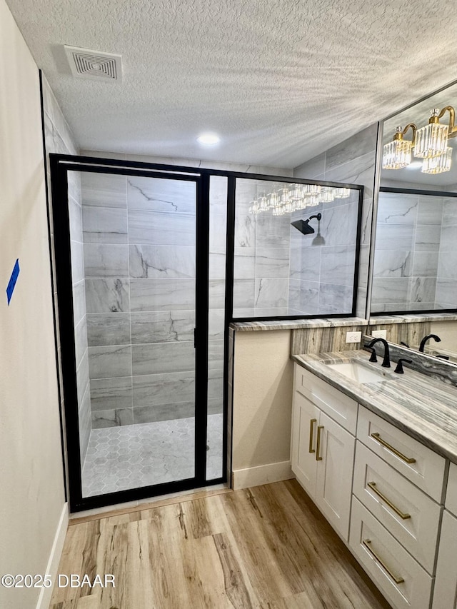 bathroom featuring a textured ceiling, a stall shower, wood finished floors, and visible vents