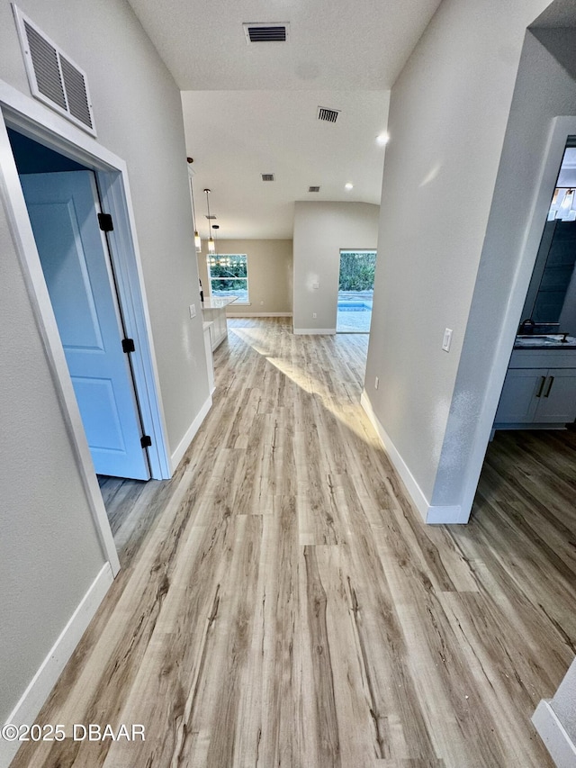 corridor with visible vents, light wood-style flooring, and baseboards