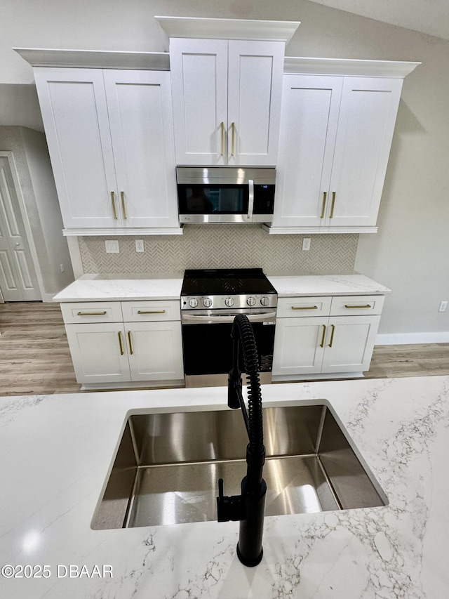 kitchen featuring stainless steel appliances, light stone counters, decorative backsplash, and white cabinets