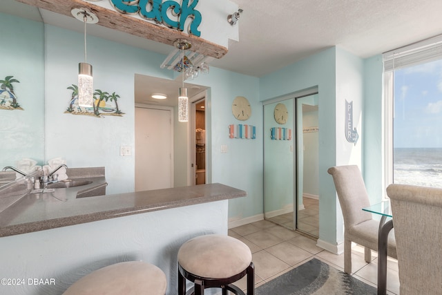 kitchen featuring light tile patterned flooring, sink, kitchen peninsula, a textured ceiling, and pendant lighting