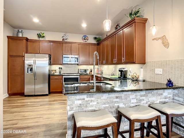 kitchen with kitchen peninsula, hanging light fixtures, light wood-type flooring, appliances with stainless steel finishes, and dark stone countertops