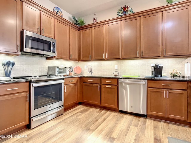 kitchen with dark stone counters, light wood-type flooring, decorative backsplash, and stainless steel appliances