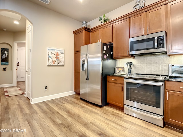 kitchen with light hardwood / wood-style floors, dark stone countertops, decorative backsplash, and appliances with stainless steel finishes