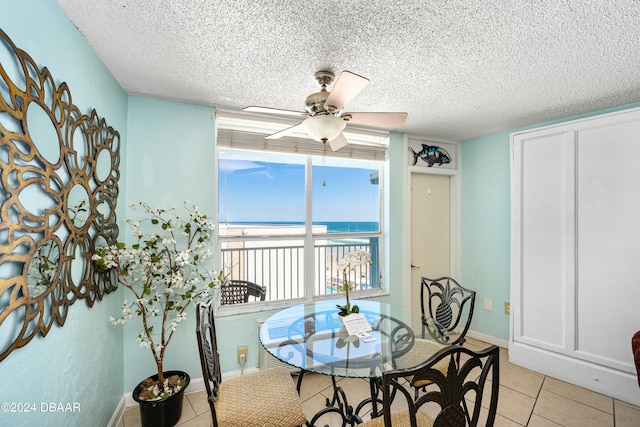 tiled dining space with a water view, a textured ceiling, and ceiling fan