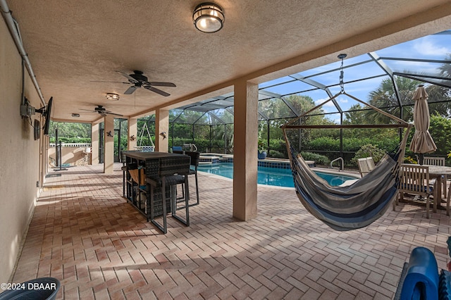 view of swimming pool featuring glass enclosure, ceiling fan, an in ground hot tub, and a patio