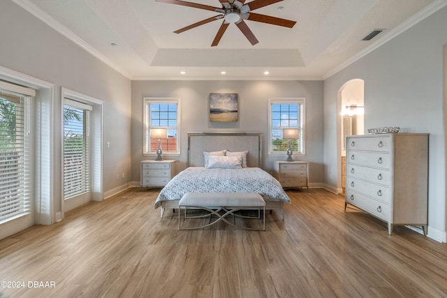 bedroom with ceiling fan, a raised ceiling, multiple windows, and light hardwood / wood-style flooring