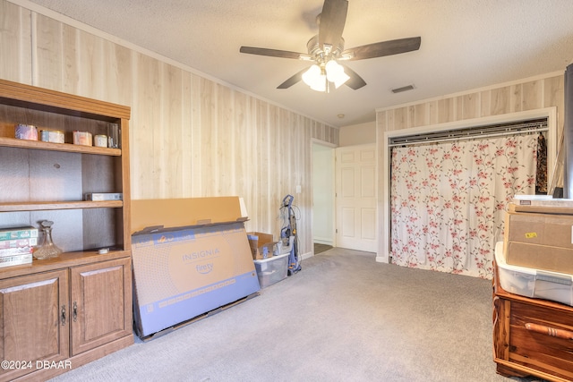 misc room featuring ceiling fan, light colored carpet, a textured ceiling, and wood walls