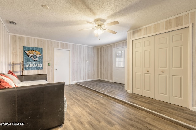 unfurnished living room with hardwood / wood-style flooring, ceiling fan, wooden walls, and a textured ceiling