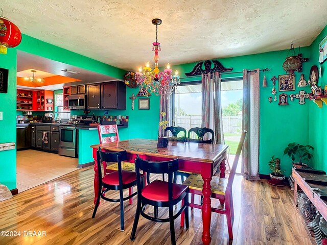 dining space featuring light wood-type flooring, a textured ceiling, and an inviting chandelier