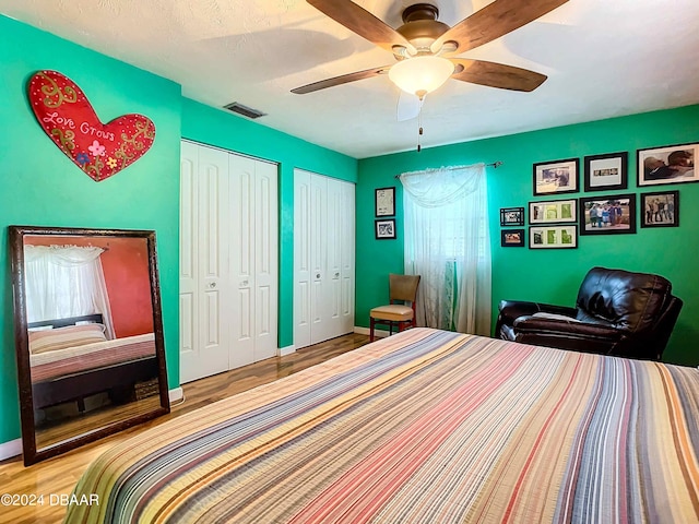 bedroom with multiple closets, light wood-type flooring, and ceiling fan