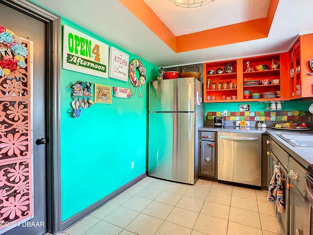 kitchen with stainless steel appliances, light tile patterned floors, backsplash, stainless steel counters, and a tray ceiling