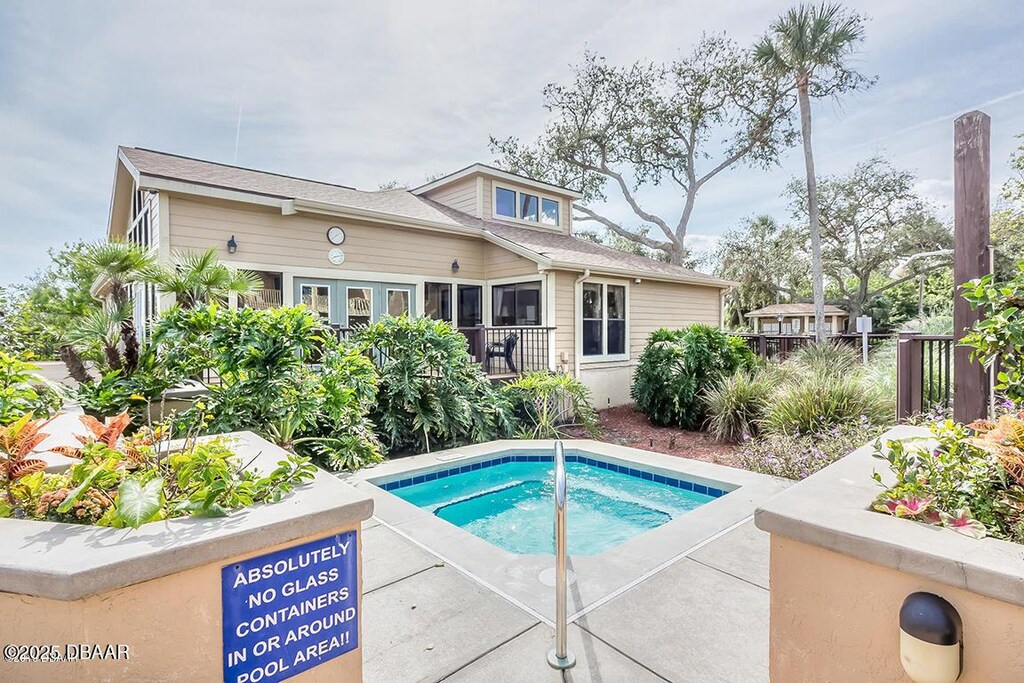 rear view of property featuring an in ground hot tub