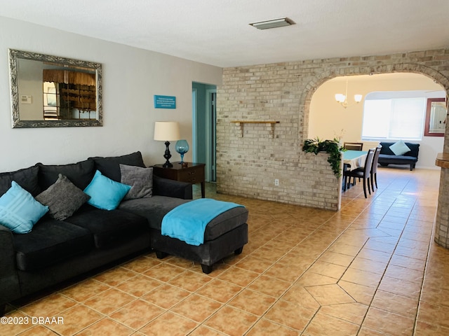 living room featuring brick wall, light tile patterned floors, and an inviting chandelier