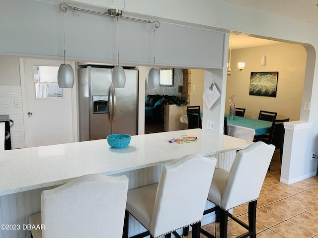 kitchen with a breakfast bar area, stainless steel fridge, hanging light fixtures, and light tile patterned floors