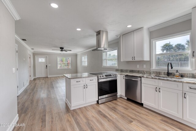 kitchen with stainless steel appliances, white cabinetry, sink, wall chimney range hood, and light wood-type flooring