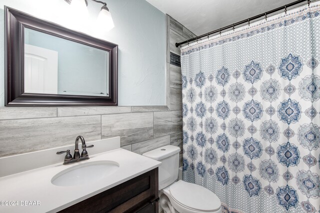 bathroom with a shower with curtain, vanity, toilet, and tile walls