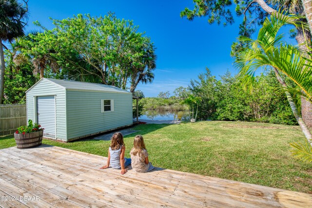 wooden terrace with a water view, a lawn, and a shed