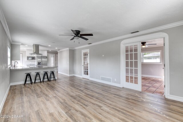 unfurnished living room featuring ceiling fan, light wood-type flooring, french doors, and ornamental molding